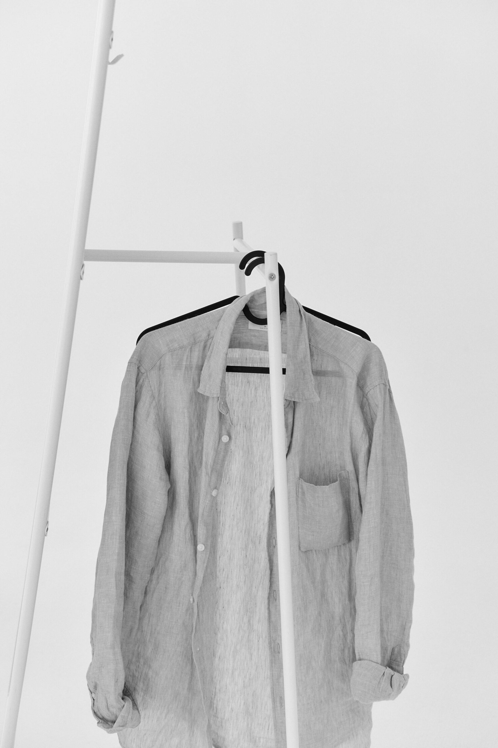 A linen shirt hangs on a sleek white rack in a minimalist setting.